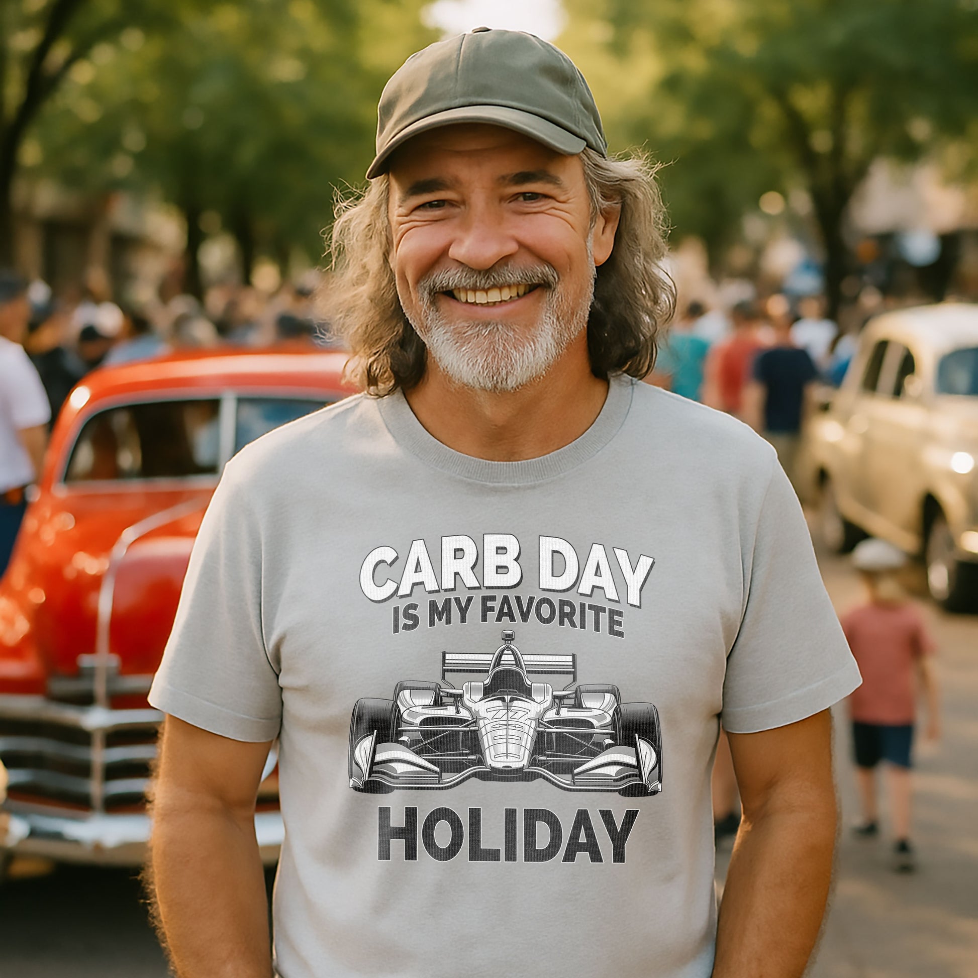 Smiling man wearing gray Carb Day Is My Favorite Holiday t-shirt at a car show with classic cars in the background