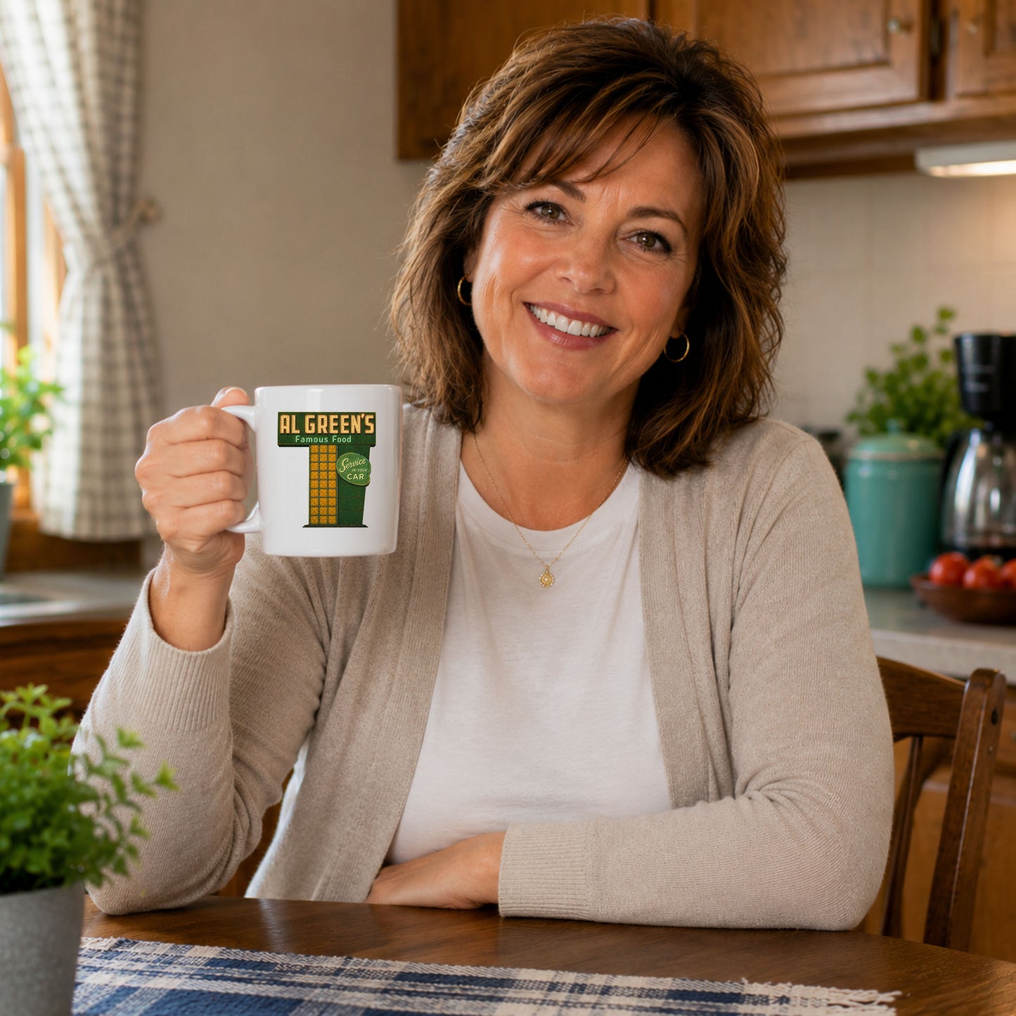 Middle-aged woman smiling at her kitchen table while holding a white coffee mug featuring a vintage Al Green’s Famous Food Indianapolis drive-in restaurant sign design.