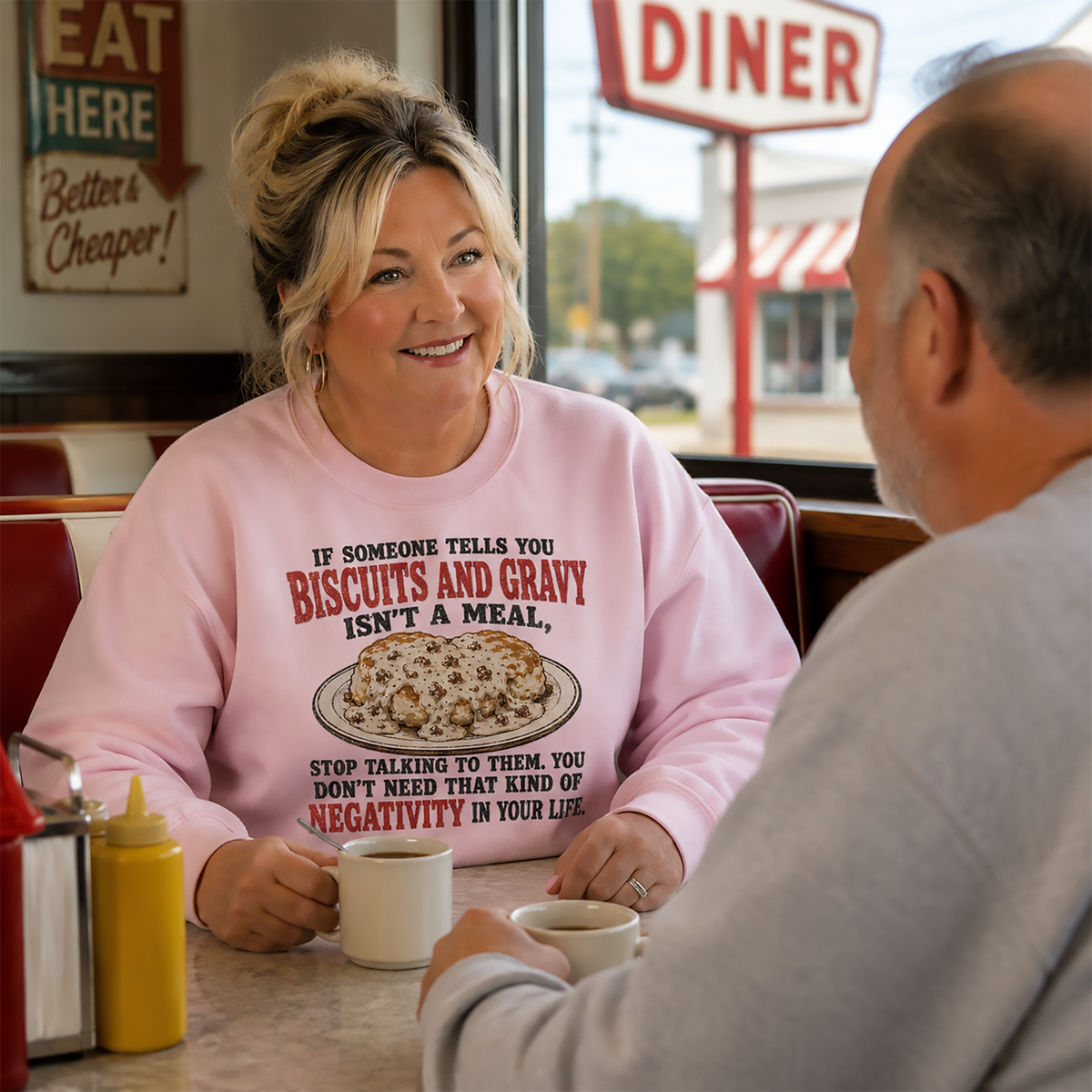Woman wearing a pink biscuits and gravy Gildan 18000 sweatshirt while having coffee with a man in a vintage-style Indiana diner.