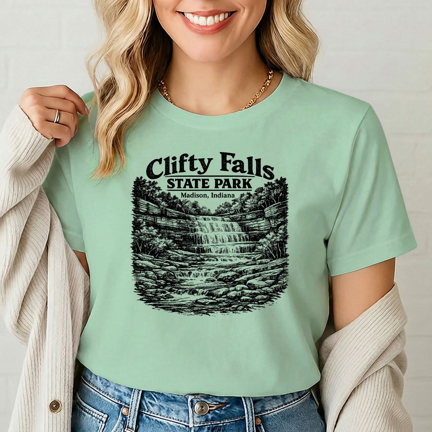 Female model showcasing Clifty Falls Madison Indiana shirt in casual pose by white wall