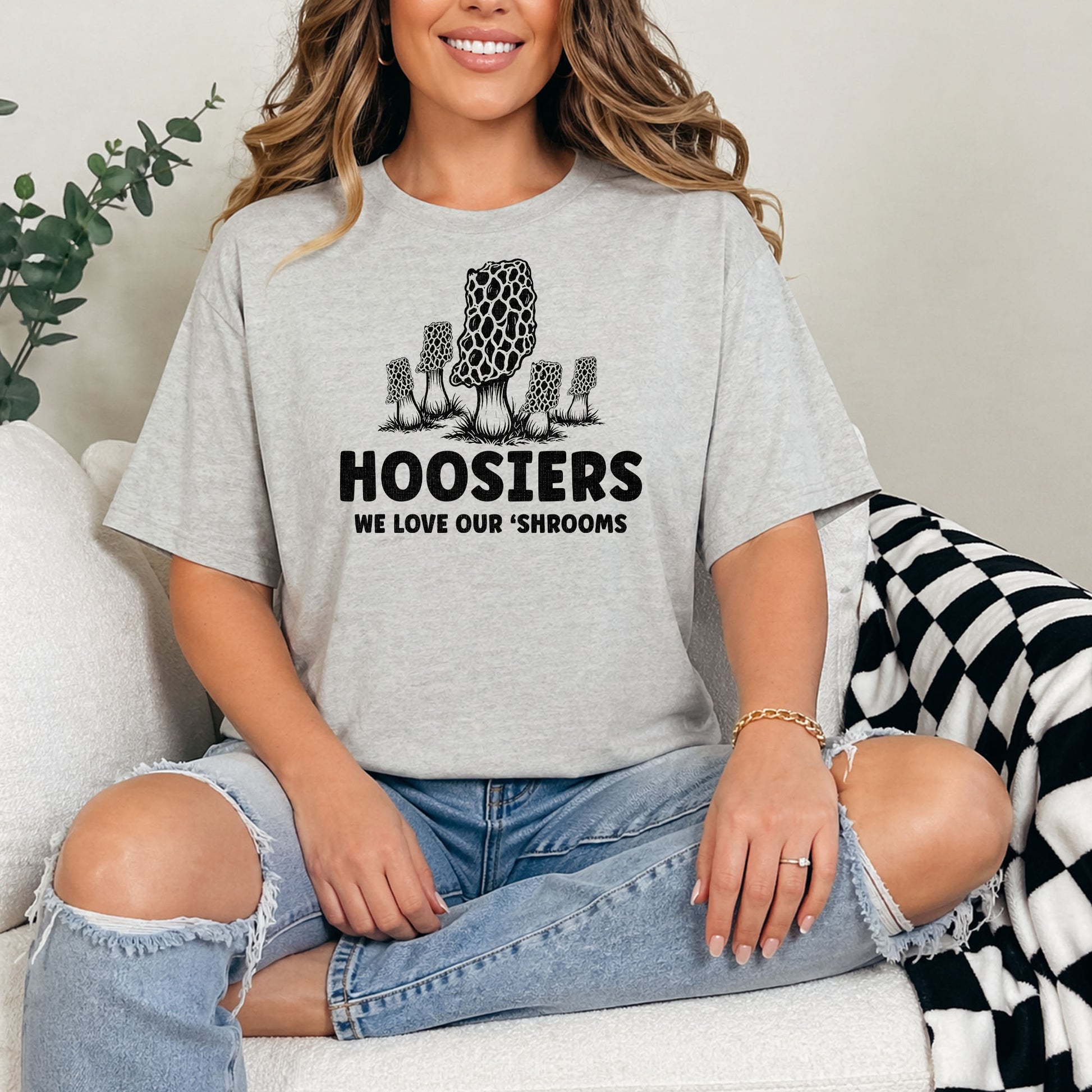 Female model wearing Indiana mushroom hunting t-shirt against white brick background