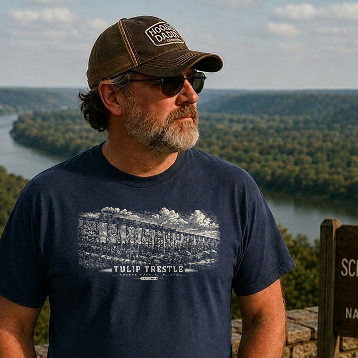 Older man standing at an Indiana scenic overlook wearing a chocolate brown t-shirt featuring a vintage engraved illustration of the Tulip Trestle railroad bridge in Greene County, Indiana.