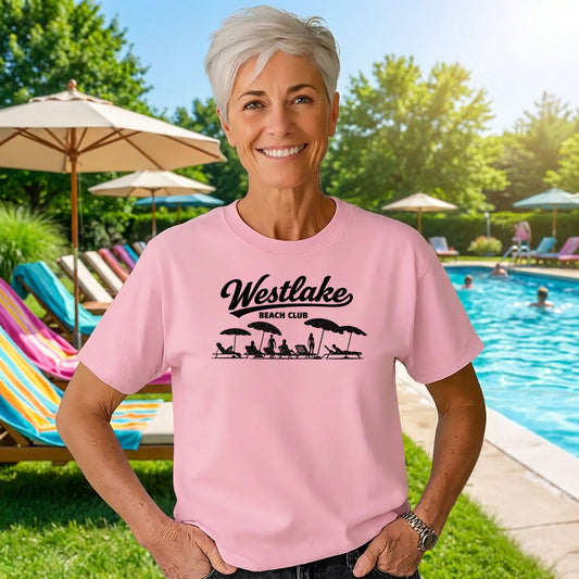Woman wearing pink Westlake Beach Club t shirt standing by outdoor pool on sunny day
